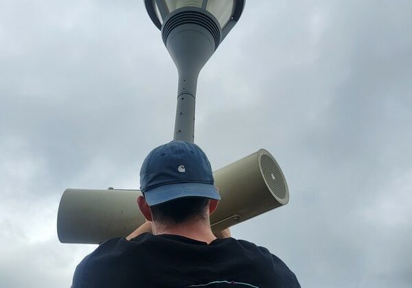 Technicien de Symbiose Organisation installant un haut-parleur sous un lampadaire par temps nuageux.