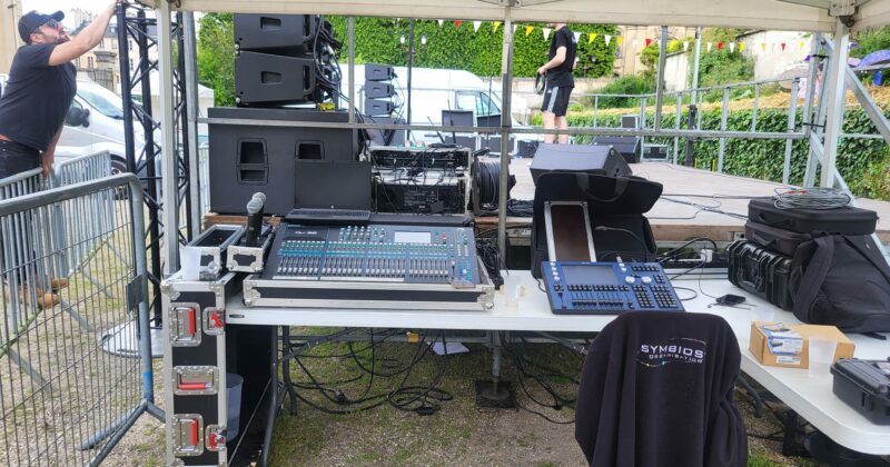 Installation de matériel de son et éclairage sous un abri, avec des équipements audio et un technicien en action.