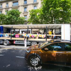 Camion de Sonorisation décoré de ballons, stationné en pleine rue, avec des personnes et du matériel de sono visible.