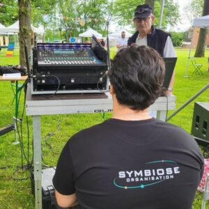 Technicien de sono de Symbiose Organisation devant une table de mixage lors d'un événement extérieur.