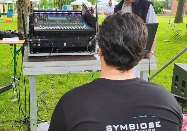 Technicien de sono de Symbiose Organisation, devant une table de mixage, préparant un événement en extérieur.