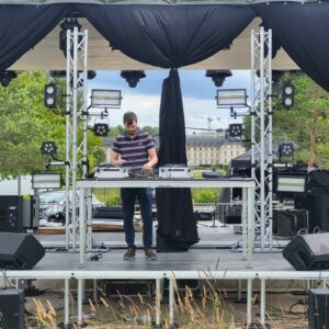 DJ en action sur une scène équipée de matériel de sonorisation et d'éclairage, prêt pour un événement.