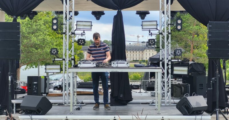 DJ en action sur une scène équipée de matériel de sonorisation et d'éclairage, prêt pour un événement.