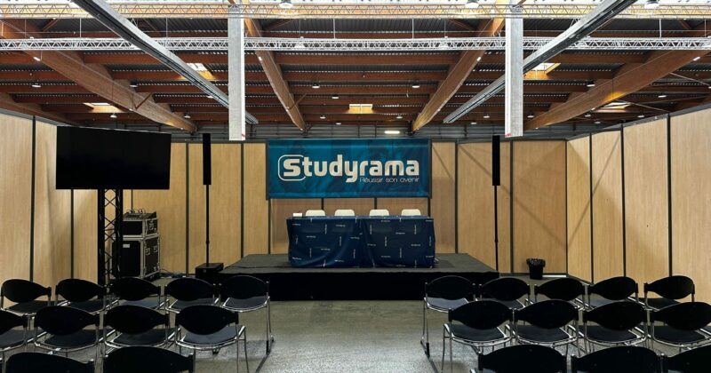 Scène vide avec des chaises en attente, panneau "Studyrama" en arrière-plan, et un écran sur le côté.