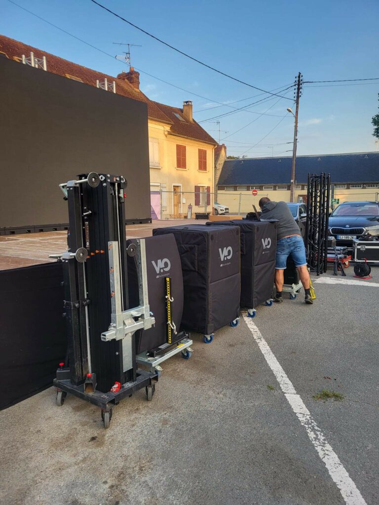 Installation de matériel de sono et éclairage sur un site, avec un technicien réglant les équipements.