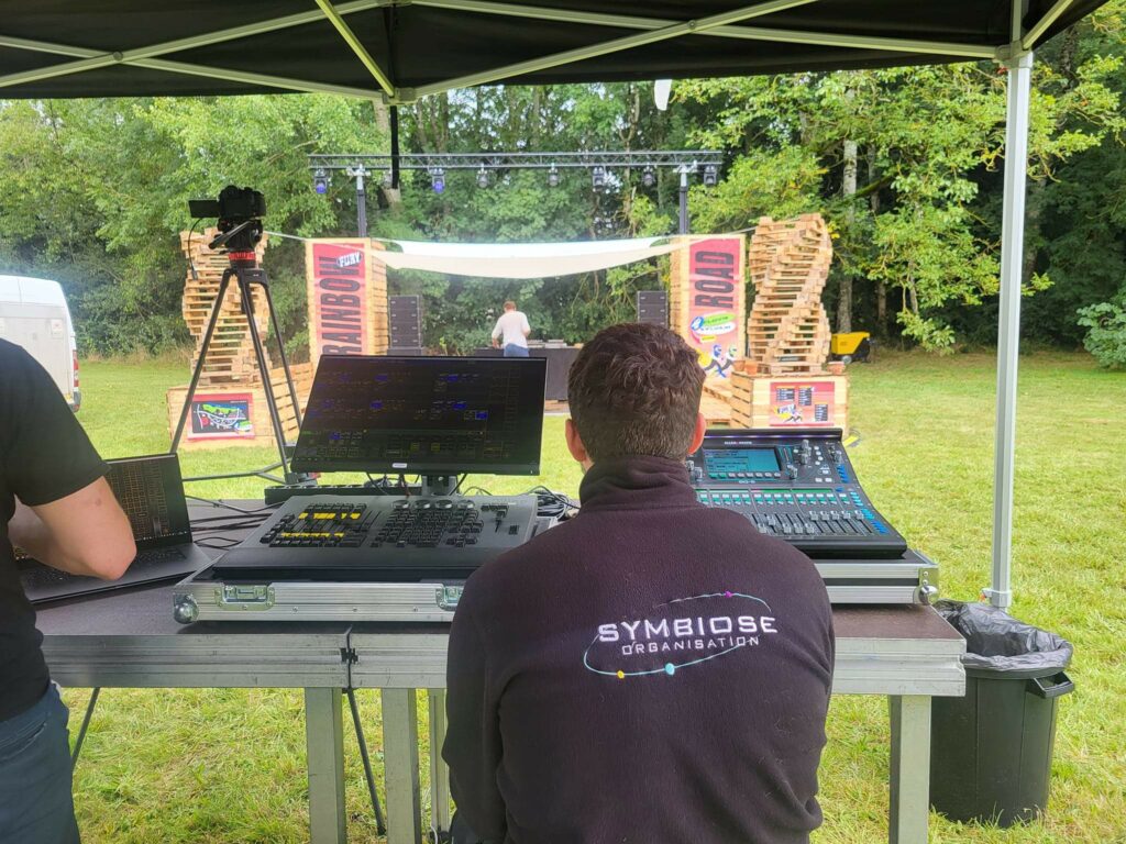 Technicien de son gérant des équipements audio et lumière pour un événement en plein air, avec une scène en arrière-plan.