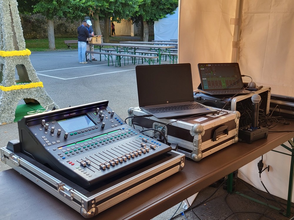 Matériel de sonorisation et d'éclairage installé sur une table, avec une table de mixage, un ordinateur et un microphone.