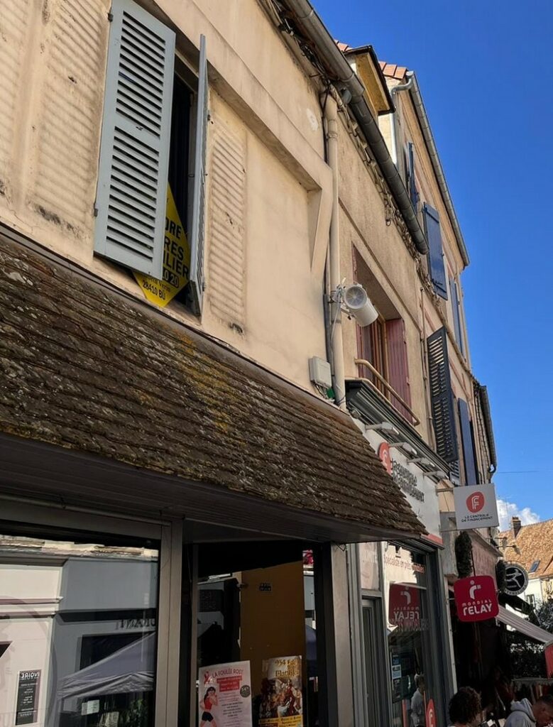 Vue de la façade d'un bâtiment, avec des volets fermés et un matériel de sonorisation installé près d'une fenêtre.