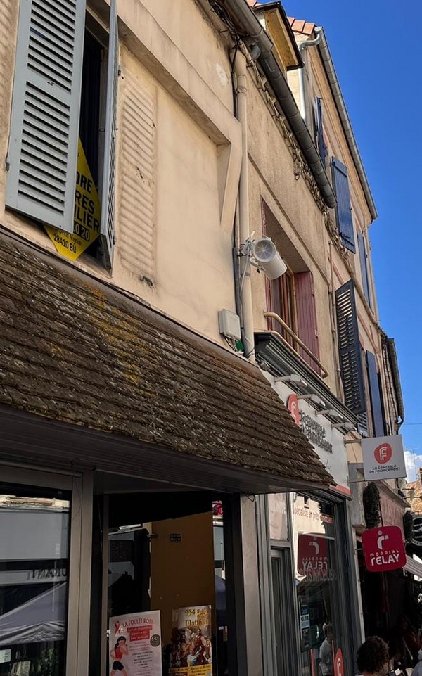 Installation de matériel de sono avec un haut-parleur fixé sur un bâtiment commercial sous un ciel ensoleillé.